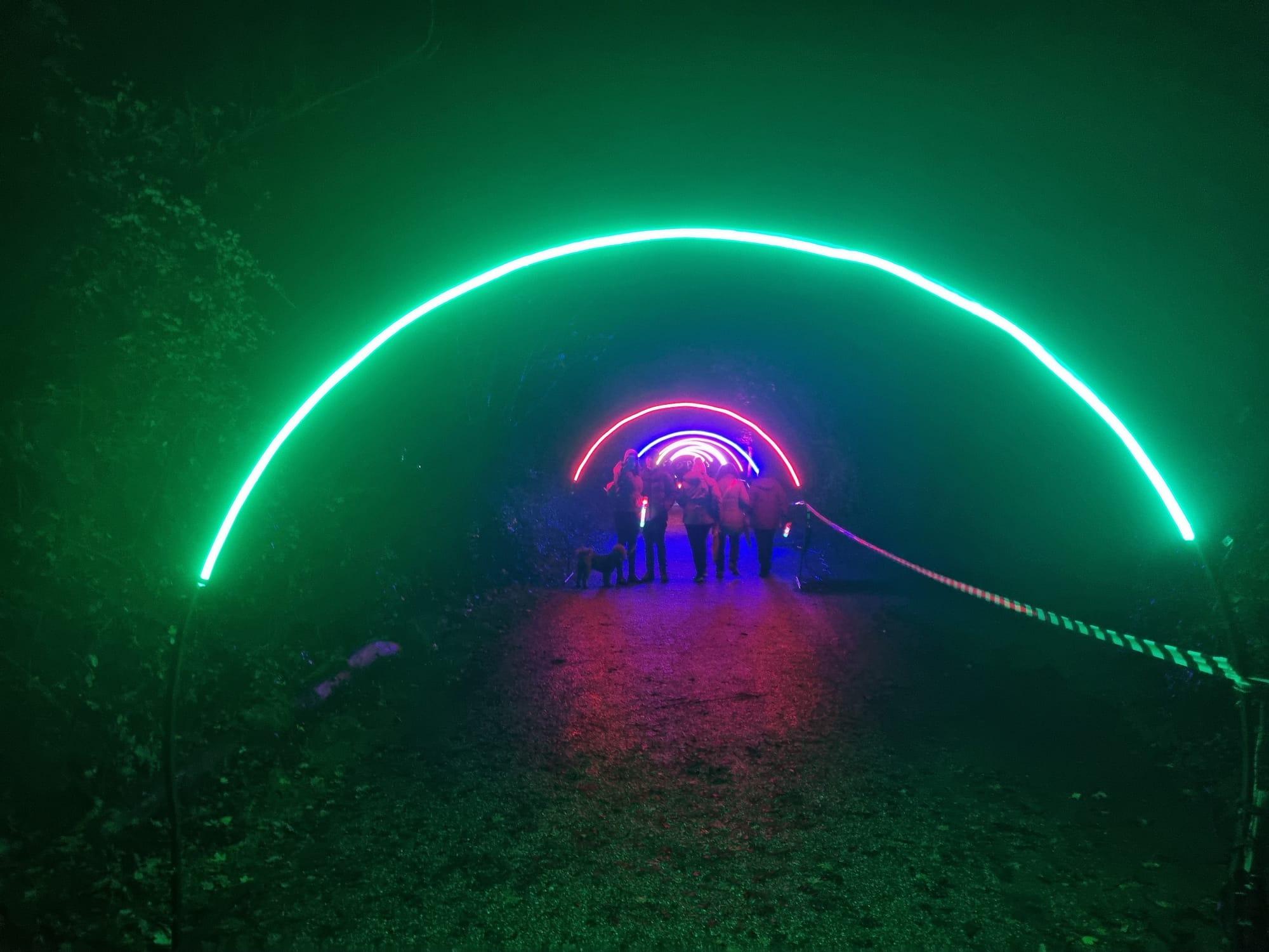 Illuminated arch tunnel installation receding down a light trail path at night